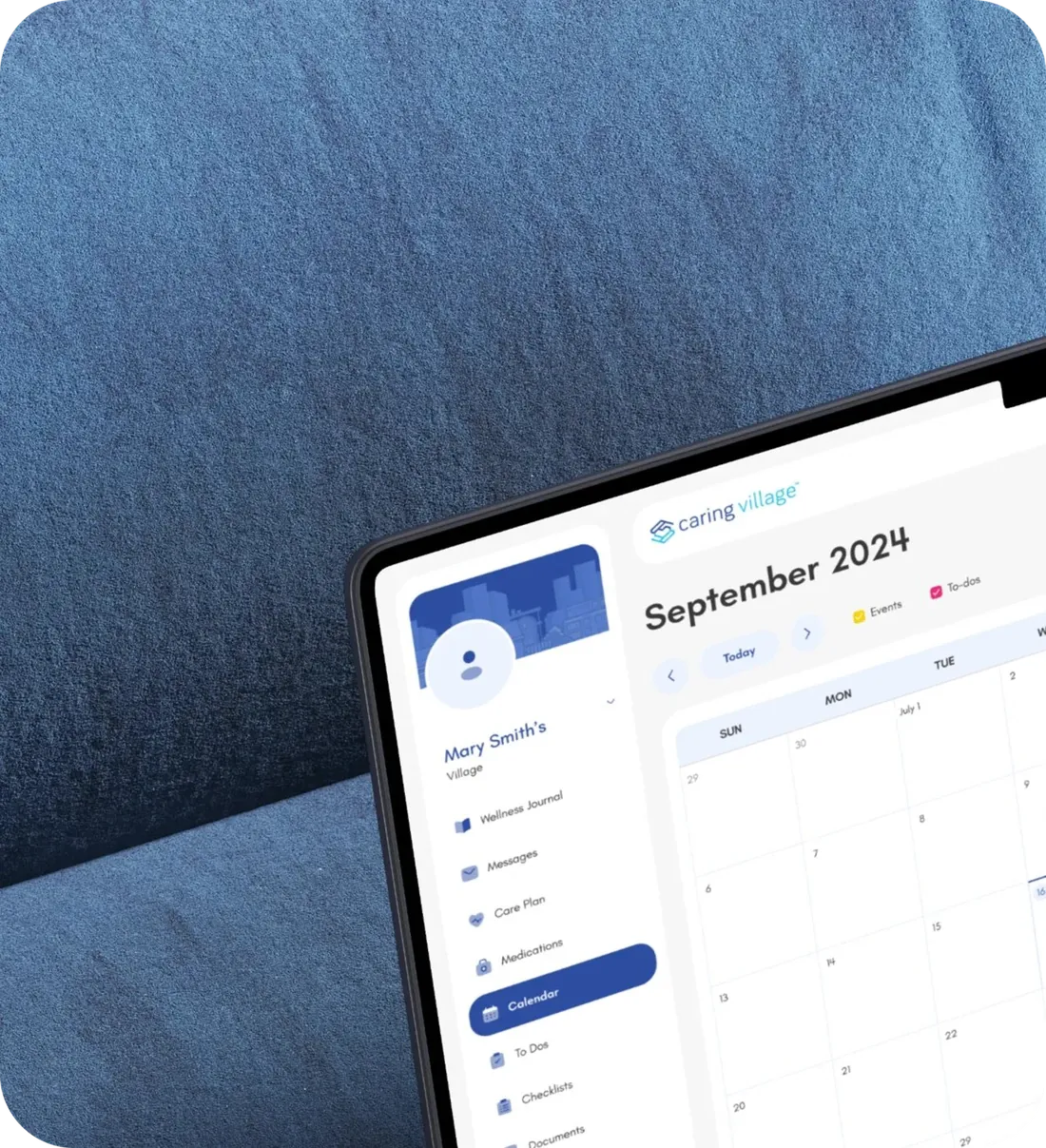 Tablet on a blue textured fabric showing the redesigned Caring Village calendar for September 2024 in Mary Smith's village.
